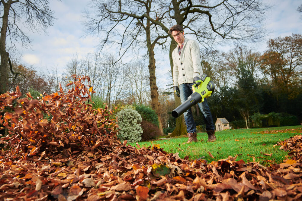 Akumulatorowa dmuchawa do liści RYOBI w trakcie pracy i usuwania mokrych liści z trawnika